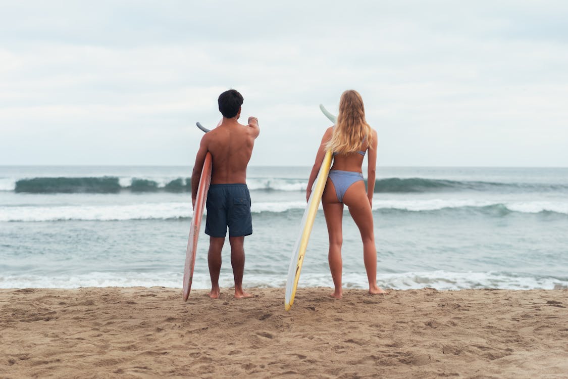 Man and Woman Holding Surfboard While Standing on the Beach