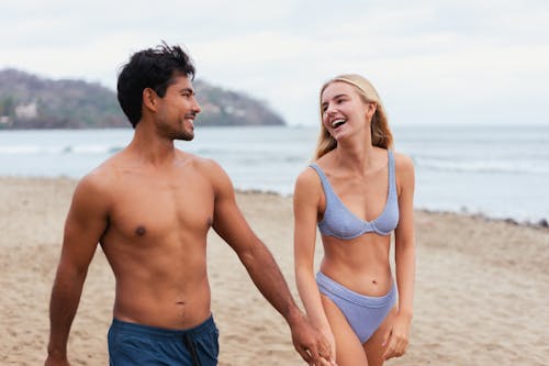 Topless Man in Shorts Walking on the Beach with Woman Wearing Bikini