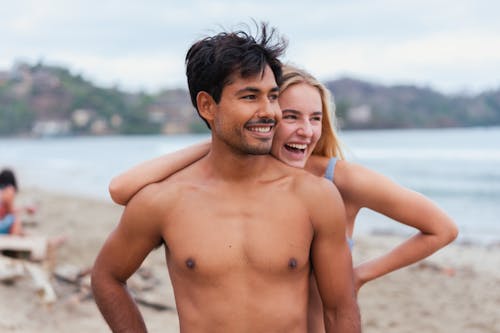 Topless Man Standing Beside Woman in Blue Bikini