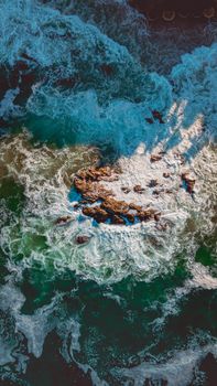 Stunning aerial view of ocean waves crashing over rocky coastline, creating a dramatic seascape.