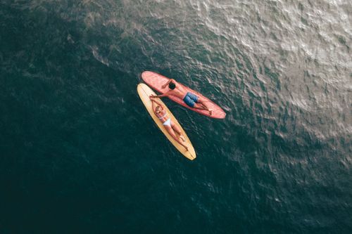 Free Drone shot of a couple on surfboards in the ocean, enjoying a sunny day. Stock Photo
