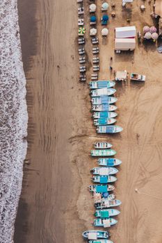 Top-down view of boats lined up along a sandy beach with umbrellas and sun loungers.