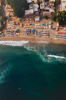 A stunning aerial view of a vibrant beach lined with colorful umbrellas and gentle waves.