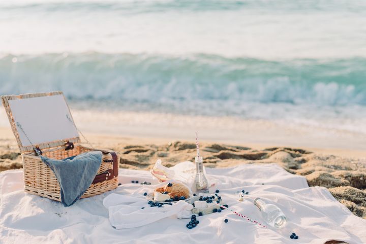 A serene beach picnic setup with a basket, blanket, croissant, and ocean view, perfect for a relaxing outing.