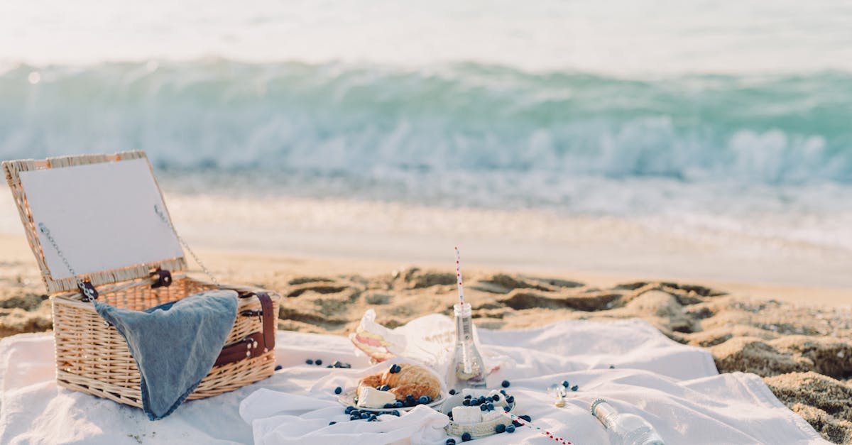 A serene beach picnic setup with a basket, blanket, croissant, and ocean view, perfect for a relaxing outing.