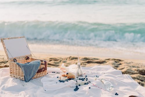 Free A serene beach picnic setup with a basket, blanket, croissant, and ocean view, perfect for a relaxing outing. Stock Photo