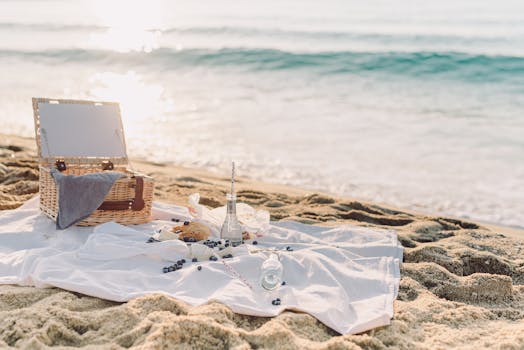 Peaceful seaside picnic setup with basket, croissant, and blueberries on a white blanket by the ocean.