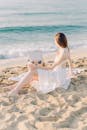 阳光明媚的日子里，一名身穿白裙的女子坐在沙滩上，凝视着海浪