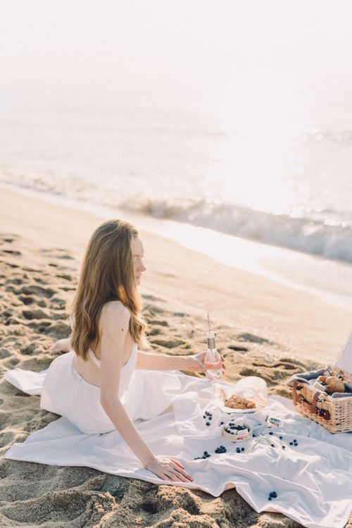 Free Elegant woman relaxing on the beach enjoying a serene summer picnic by the seashore. Stock Photo