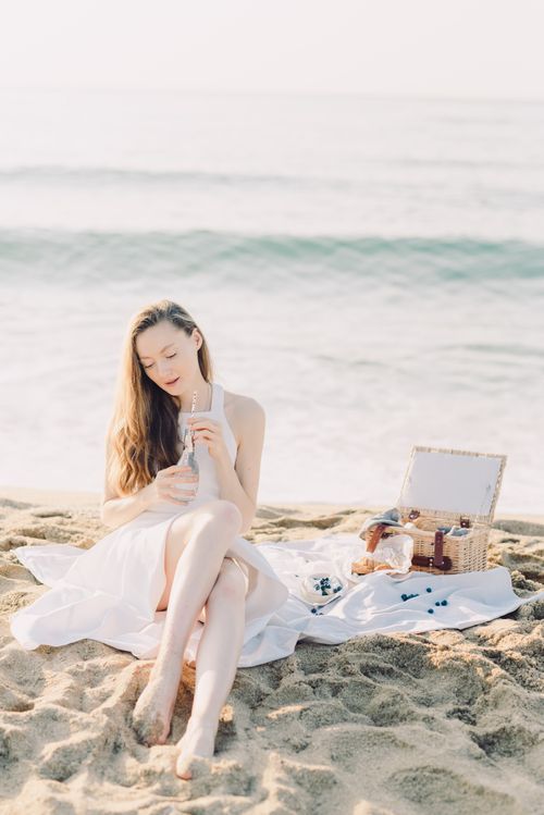 Free A serene scene of a young woman in a white dress having a picnic on a sandy beach. Stock Photo