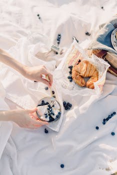 A refined picnic spread featuring croissants and fresh blueberries on a white blanket.