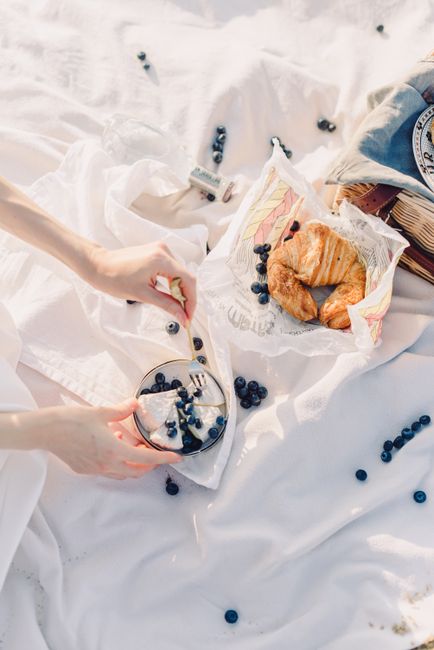 A refined picnic spread featuring croissants and fresh blueberries on a white blanket.