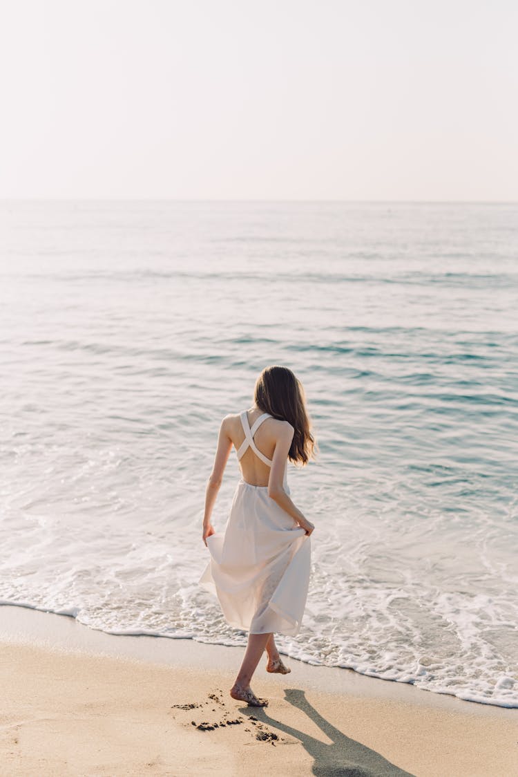 A Woman In White Dress Walking On The Beach