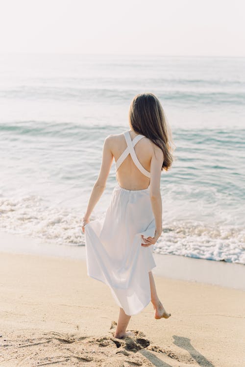 Woman Holding Her Dress While Walking on the Beach