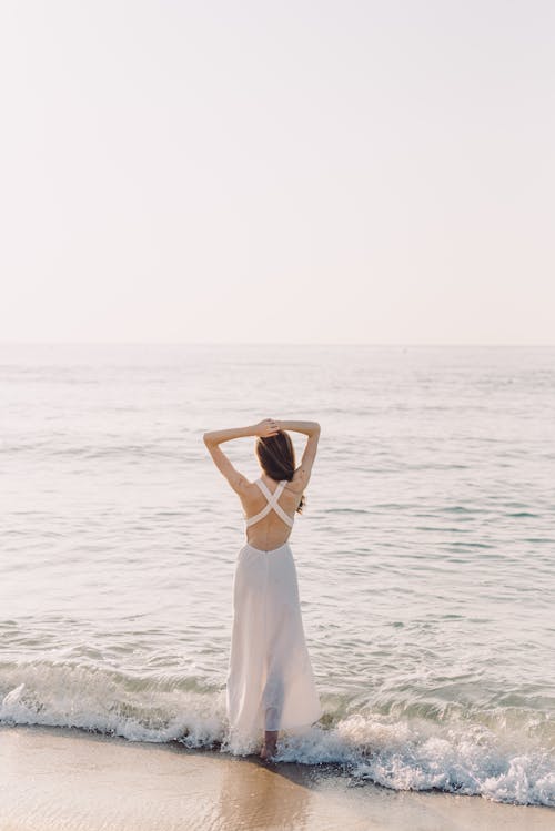 Free Woman Standing on Crashing Waves on the Shore Stock Photo