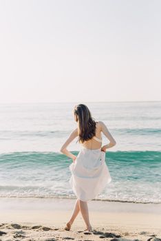 Woman in white dress enjoying the peaceful beach at sunrise, creating a serene summer vibe.