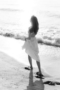 A serene morning beach walk captures a woman in a flowing white dress enjoying the waves.