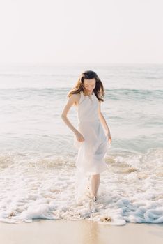 Elegant woman in a white dress walking along the beach during sunrise.