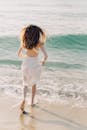 穿着白色连衣裙的女人走在阳光明媚的海滩上，享受海浪