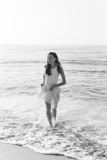 Black and white photo of a woman in a white dress enjoying a stroll in the sea waves.