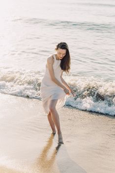 A woman in a white dress enjoying a walk on a sunny beach with gentle waves.