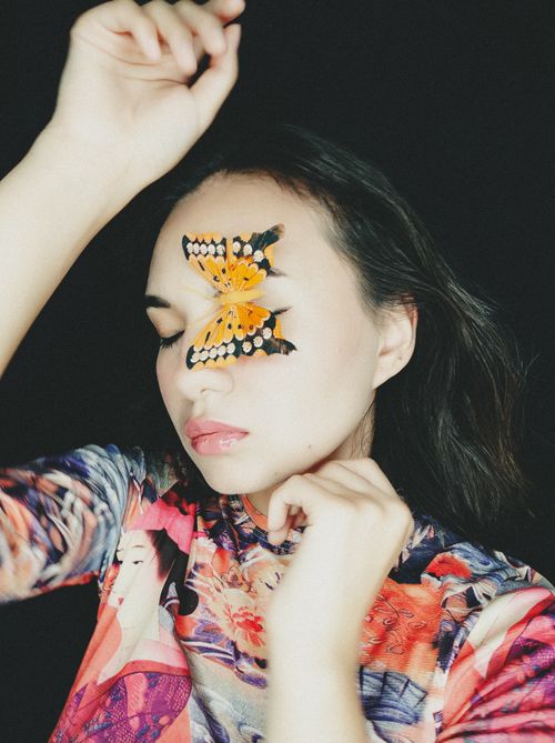 Free Artistic portrait of a woman with a butterfly on her face against a black background. Stock Photo