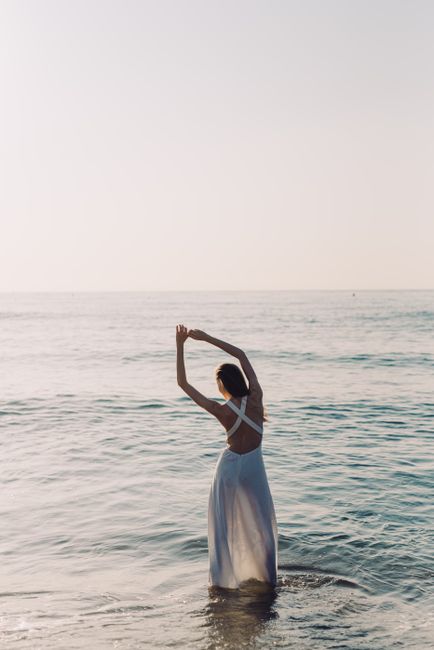 Elegant woman in a dress standing in the ocean at sunrise, embracing tranquility.