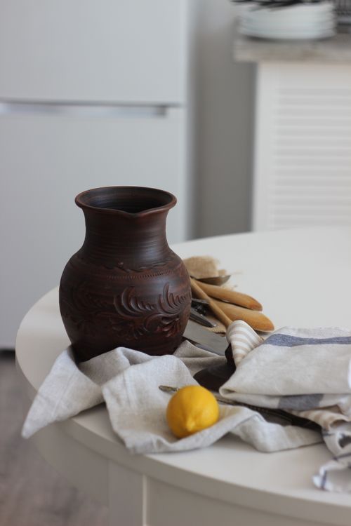 Free A rustic clay jug on a kitchen table amidst cloths and utensils, creating an earthy decor theme. Stock Photo