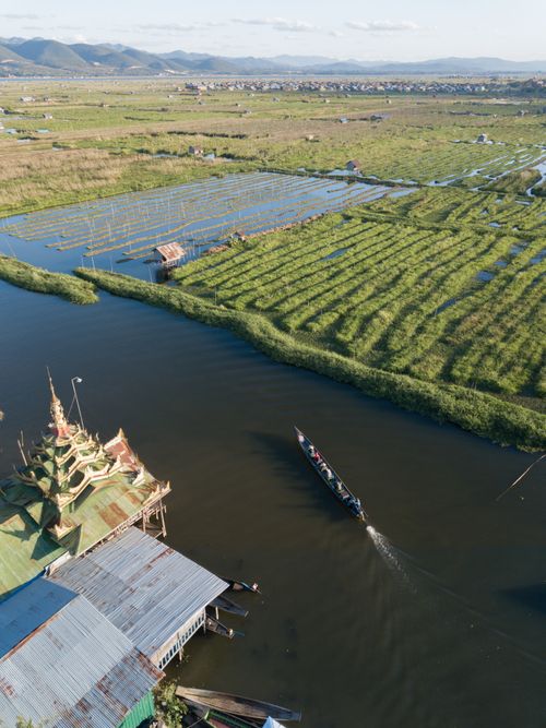 Free A serene aerial shot of a boat navigating through floating gardens and temples in Shan State, Myanmar. Stock Photo