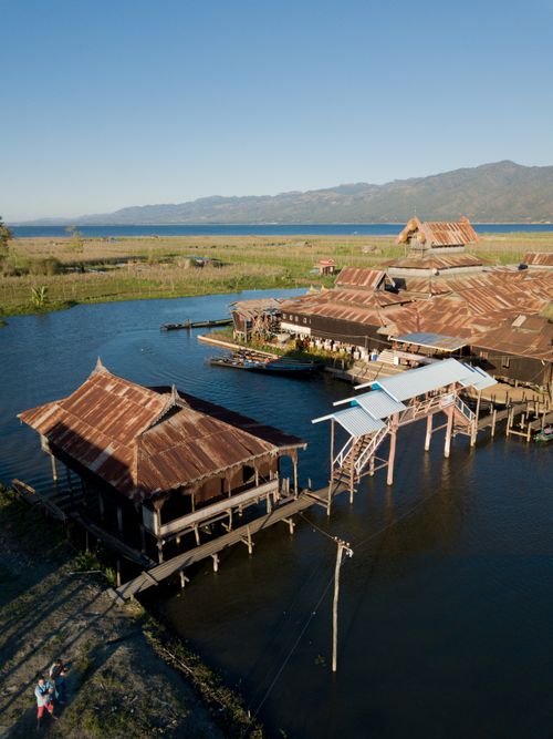 Free Stunning aerial shot of traditional floating houses on Inle Lake, Myanmar with mountainous backdrop. Stock Photo