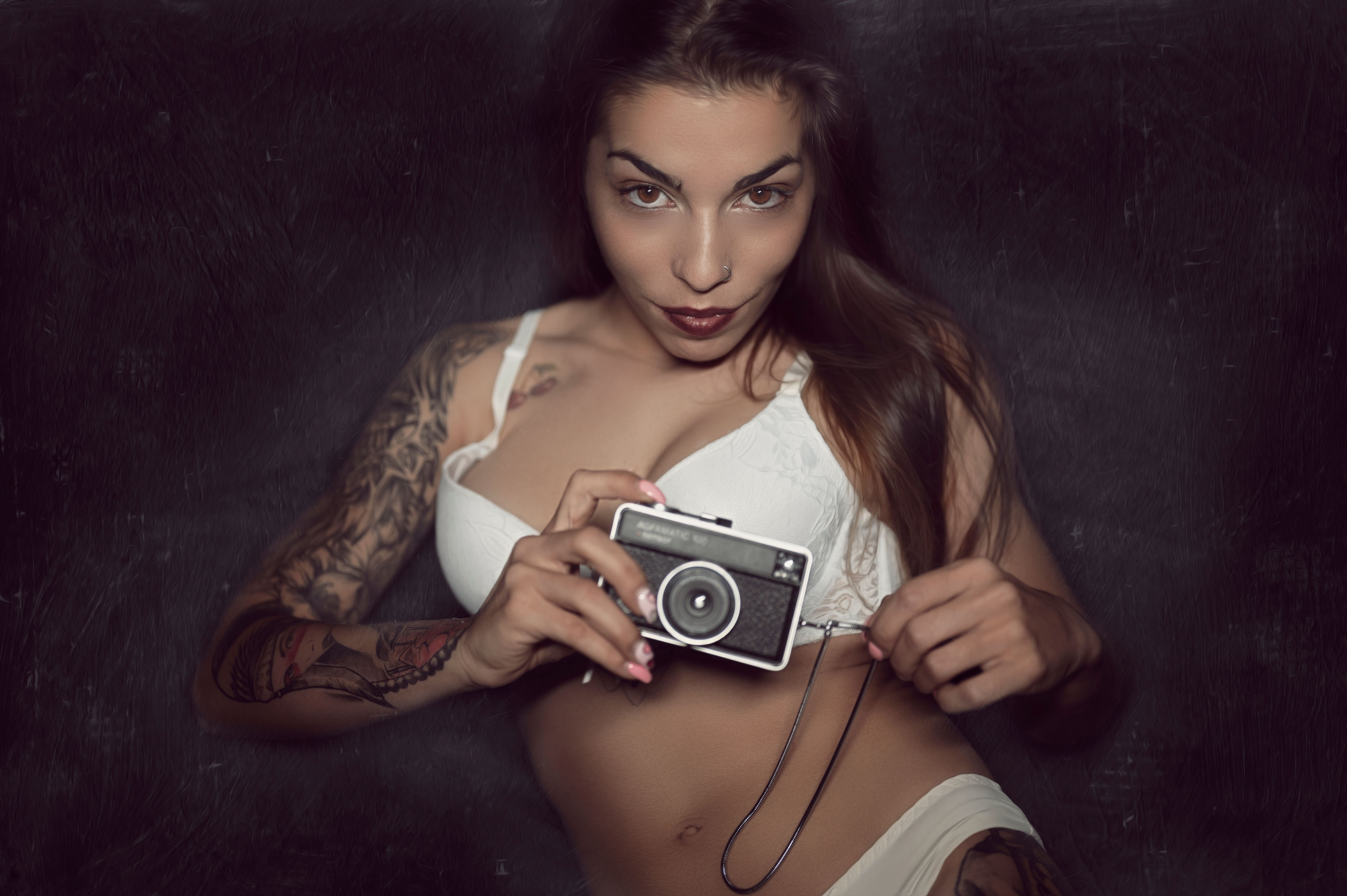 Portrait of a tattooed woman holding a vintage camera in a studio setting.