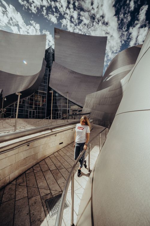 Free A woman walking on a modern architectural pathway with sweeping metal surfaces under a bright sky. Stock Photo