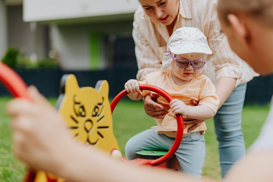 A playful moment between mother and child on a colorful playground seesaw outdoors.