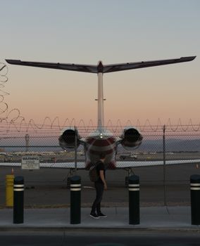 A traveler at airport fence watching a plane during dusk in Las Vegas.