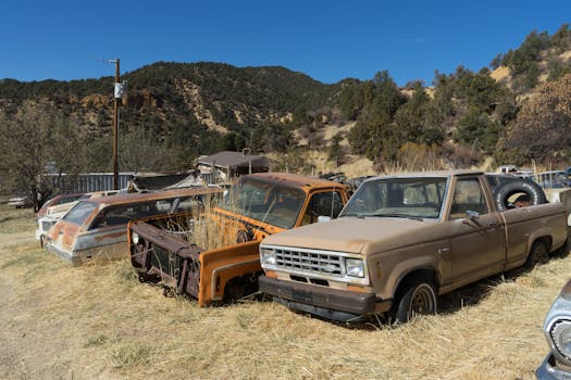 A collection of vintage vehicles rusting in a rural American junkyard.