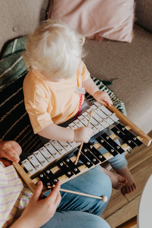 Free A young child sitting on a sofa plays a xylophone with adult supervision. Stock Photo