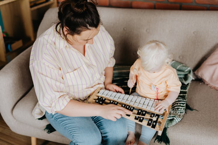 Mother And Child Sitting On Sofa Playing Xylophone