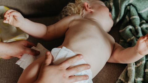 A nurturing moment of a mother changing her baby's diaper on a cozy couch indoors.