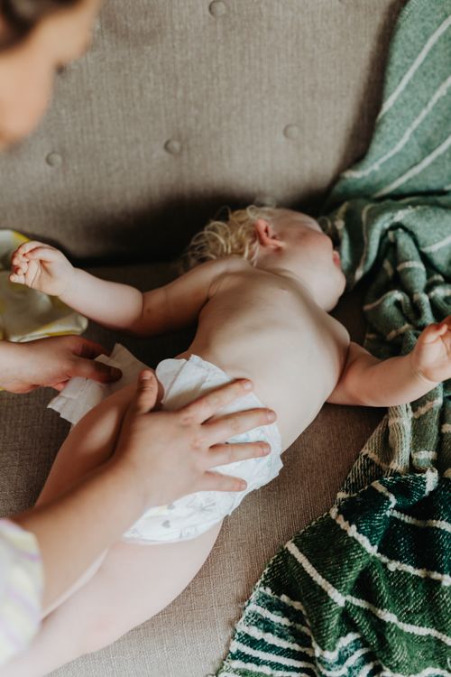 Free A nurturing moment of a mother changing her baby's diaper on a cozy couch indoors. Stock Photo