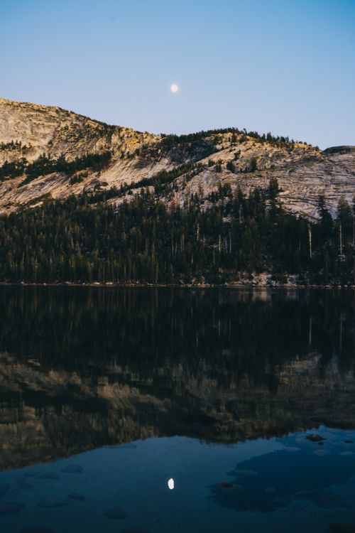 Free Peaceful landscape of a mountain lake reflecting the surrounding forest at sunset. Stock Photo