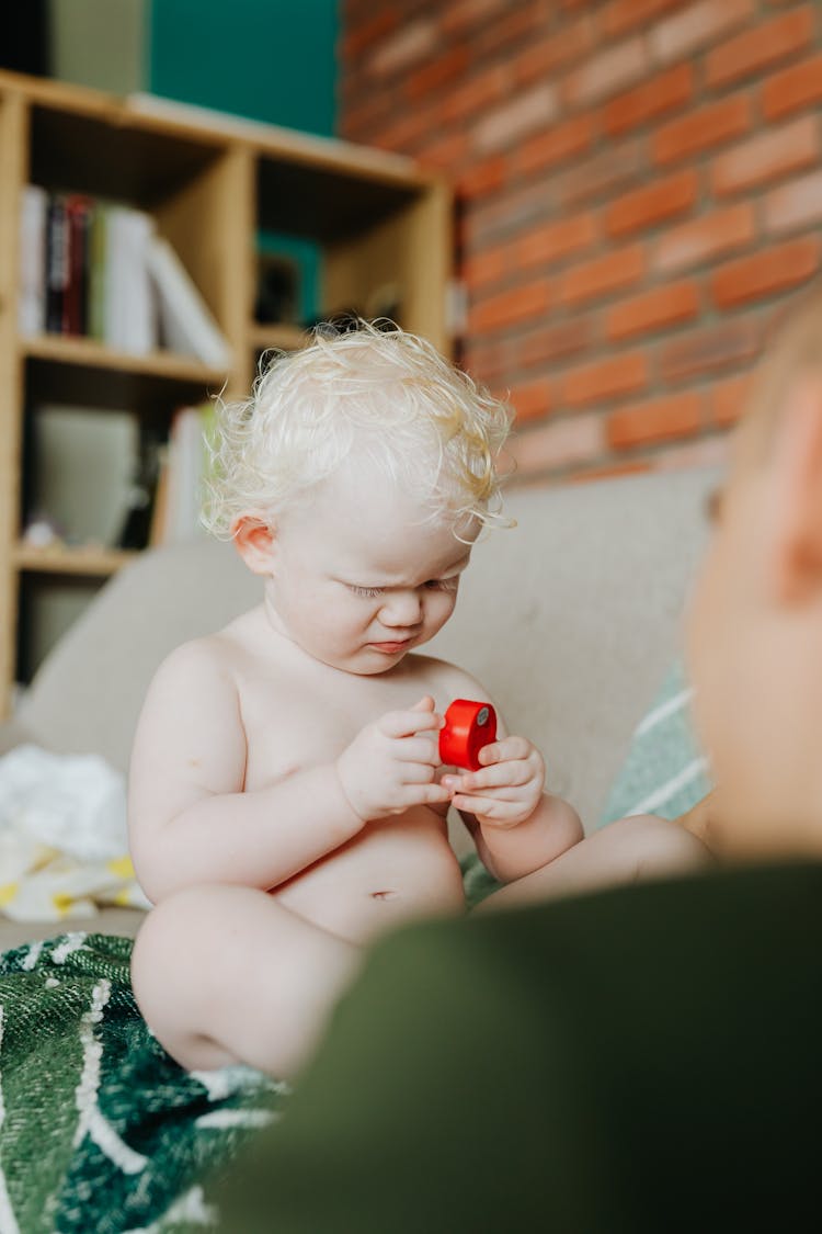 Topless Baby Sitting Holding Red Round Toy