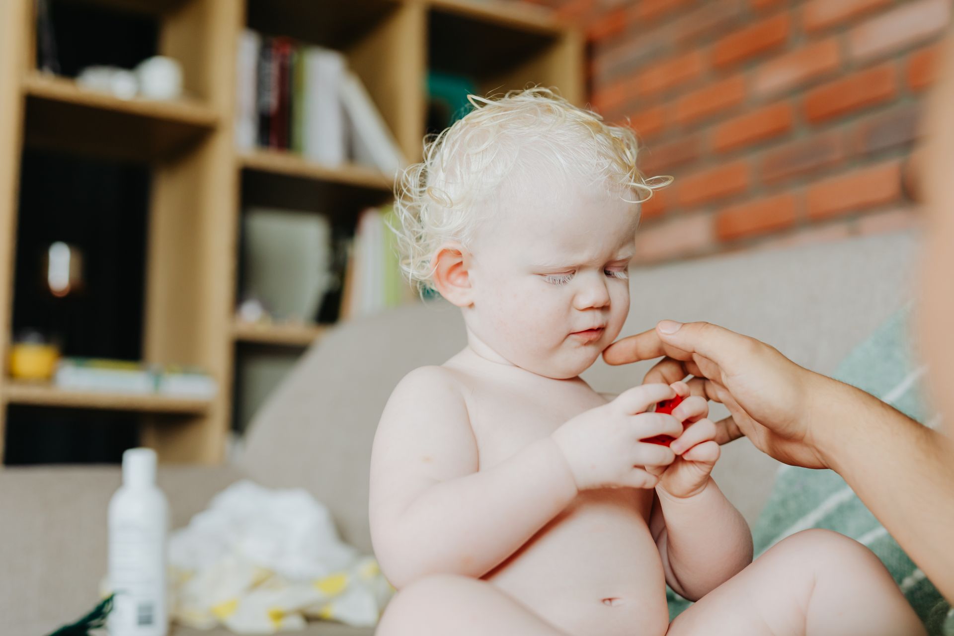 A cute albino child playing indoors, gently holding a hand, expressing tenderness.