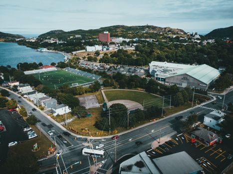 Aerial shot of a cityscape featuring a stadium, lake, and road intersection on a sunny day.