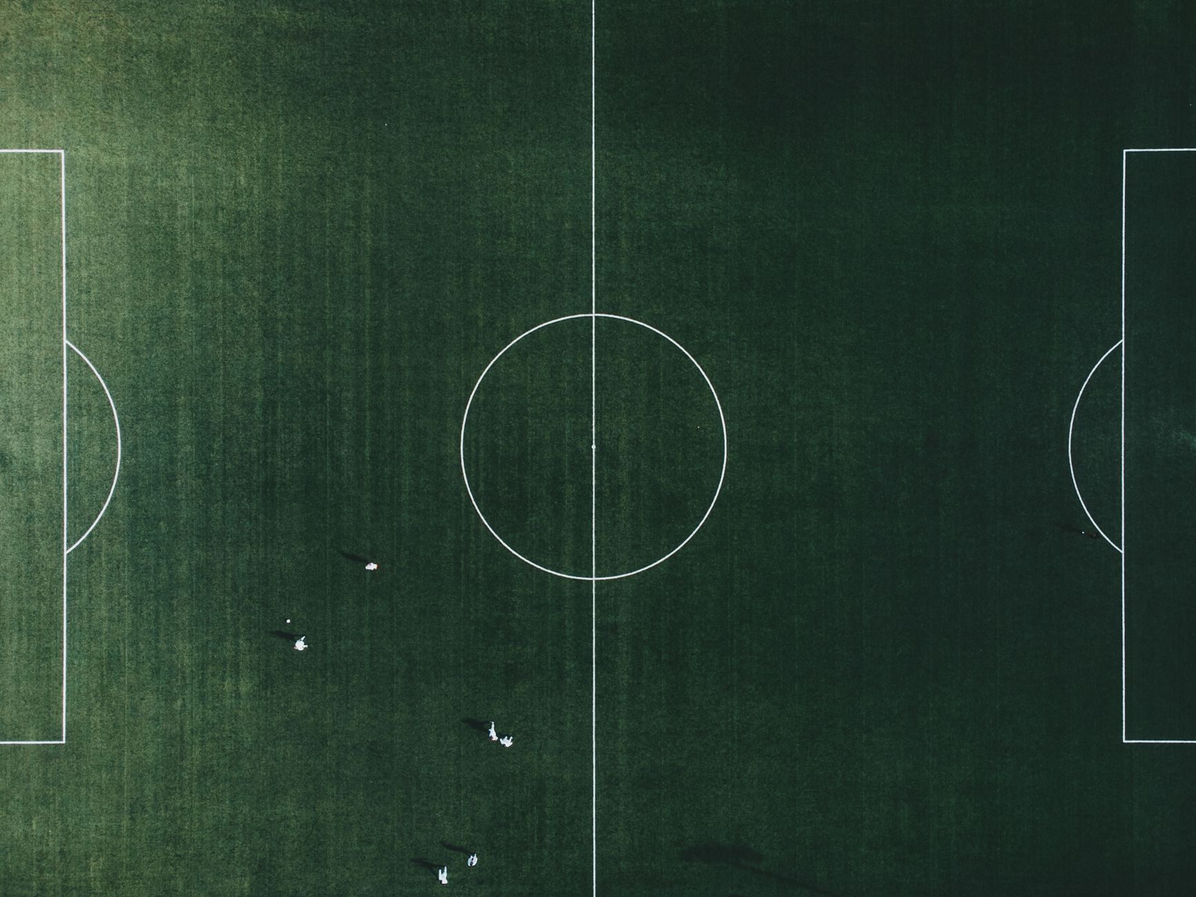 A high-angle shot of a green football field with visible lines and few players.