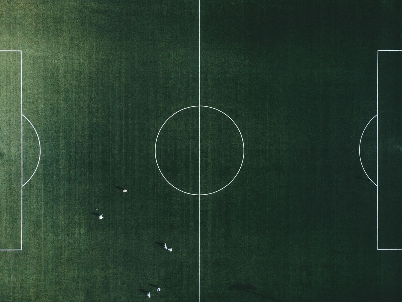 a high angle shot of a green football field with visible lines and few