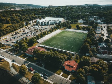 Aerial shot showcasing a soccer field in a vibrant town setting, surrounded by parking and greenery.