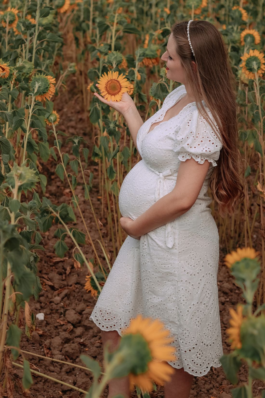 An expectant mother enjoying a quiet moment among sunflowers