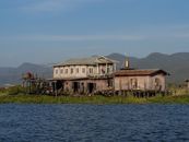 Scenic view of a traditional stilt house on Inle Lake in Myanmar with mountains in the background.