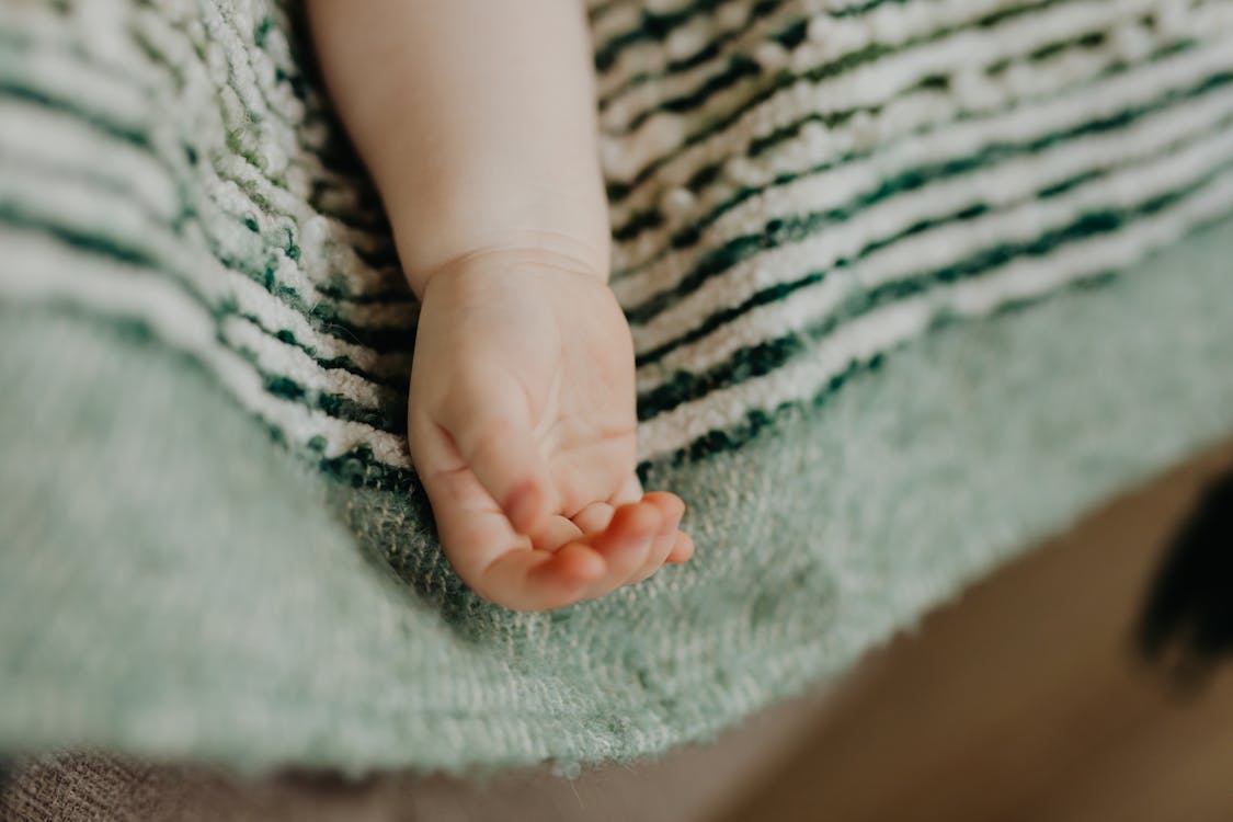 Babys Hand on White and Green Stripped Textile