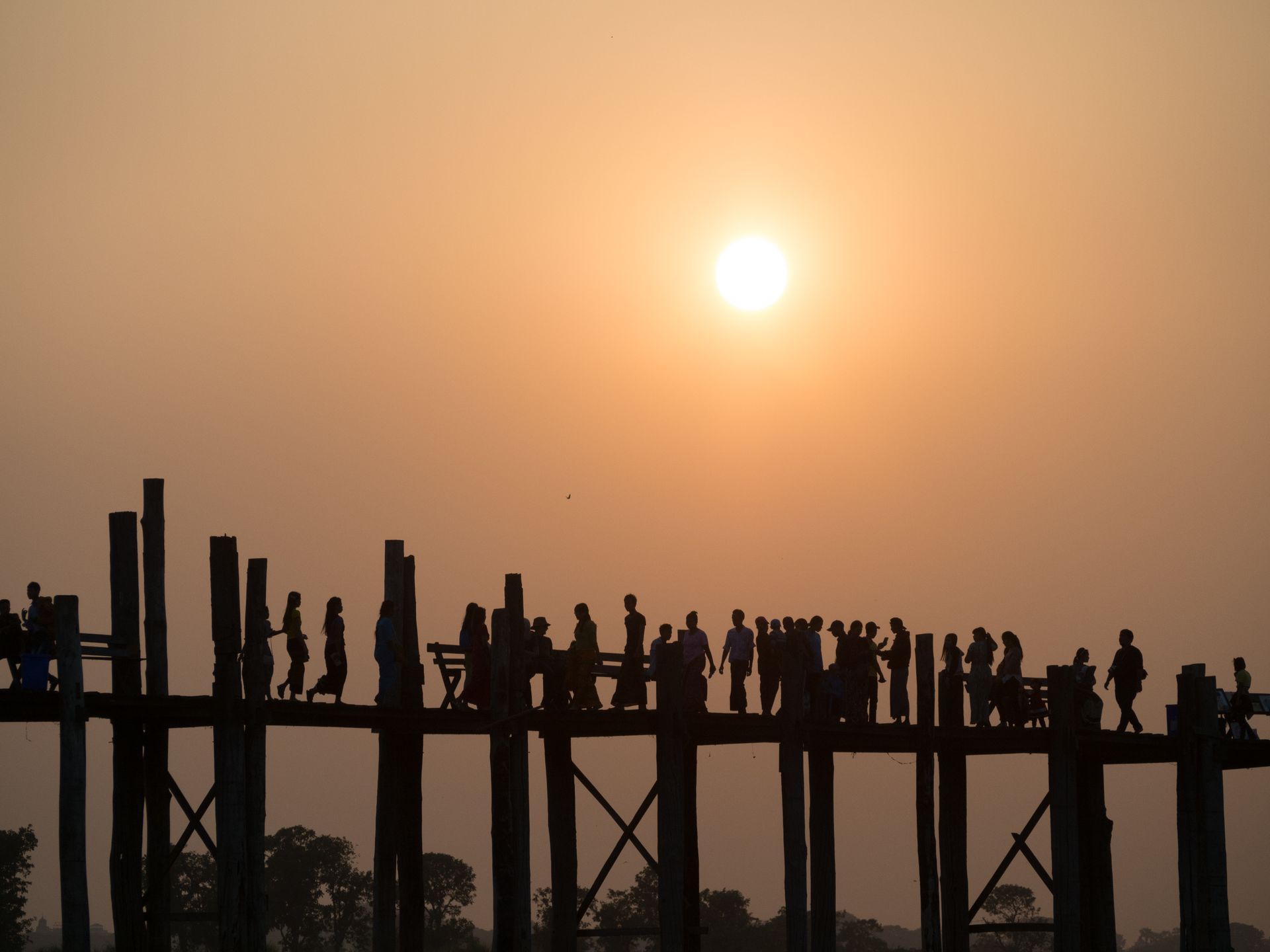 Silhouettes of people walking on U Bein Bridge, Mandalay, Myanmar during a stunning sunset.